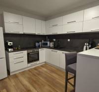 Kuchyně v 2-pokojovém bytě s bílými skříňkami a podlahou s dřevěným dekorem.