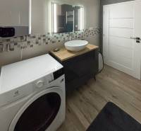 Koupelna s pračkou a umyvadlem ve 3-pokojovém bytě, malá mozaika na stěně.