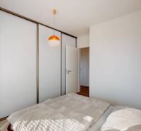 Ložnice v dvoupokojovém bytě s posuvnou skříní a postelí na podlaze s dřevěným dekorem.