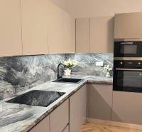 Kuchyně s tmavou pracovní deskou, vestavěnými spotřebiči a dekorativními květinami ve 4pokojovém bytě.