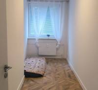 Úzký pokoj s velkým oknem a podlahou s dřevěným dekorem ve 4pokojovém bytě.