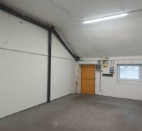 Interiér výrobních prostor s bílými stěnami a oknem s mřížkou.