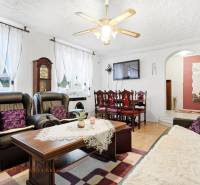 Obývací pokoj rodinného domu s krbem, černými sedačkami a podlahou s dřevěným dekorem.