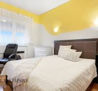 Ložnice v rodinném domě s postelí, křeslem a podlahou s dřevěným dekorem.