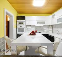 Kuchyně s bílou pracovní deskou, žlutými stěnami a moderními spotřebiči v rodinném domě.