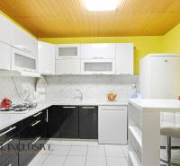 Kuchyně v rodinném domě se světlými skříňkami, mramorovým obkladem a bílými spotřebiči.