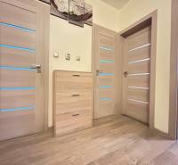 Dřevěný dekor podlahy a světlé dveře v 2-pokojovém bytě s jemným osvětlením.