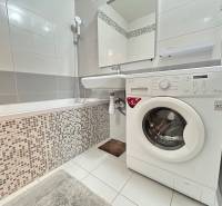 Koupelna s vanou a pračkou ve 2-pokojovém bytě, dlažba a bílé obklady.