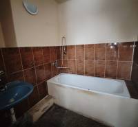 Koupelna s hnědými obklady, vanou a modrým umyvadlem v 2-pokojovém bytě.