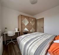 Ložnice v 3-pokojovém bytě s postelí, skříní, stolem a podlahou s dřevěným dekorem.