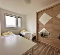 Ložnice s dvěma postelemi, bílým stolem a skříní ve 3pokojovém bytě.