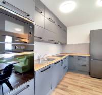 Kuchyně ve 3-pokojovém bytě s podlahou s dřevěným dekorem, šedé skříňky, vestavěné spotřebiče.