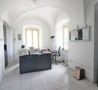 Kancelář v budově s oblými stropy, pracovní stůl a dvě okna.