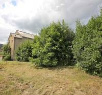 Budova ve Velkých Uhercích obklopená zelení, s výhledem na kopcovitou krajinu.