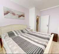 Ložnice v rodinném domě s dekorativním textilem a podlahou s dřevěným dekorem.