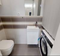 Koupelna s toaletou a pračkou v rodinném domě, světlé obklady a dlažba.