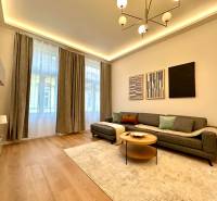 Obývací pokoj v 2-pokojovém bytě s podlahou s dřevěným dekorem, šedou sedačkou a dekorativními obrazy.