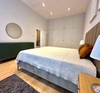 Ložnice ve 2-pokojovém bytě s postelí, skříněmi a podlahou s dřevěným dekorem.