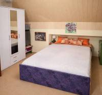 Ložnice v rodinném domě s postelí, bílou skříní a dekoracemi na stěně.