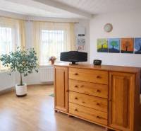 Světlý pokoj v rodinném domě s dřevěným dekorem, komodou a pokojovou rostlinou.