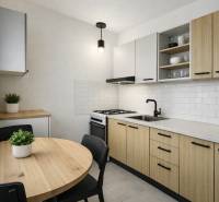 Kuchyně v 3-pokojovém bytě s dřevěným dekorem, bílými kachličkami a kulatým stolem.