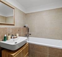 Koupelna s umyvadlem, zrcadlem a vanou v 2pokojovém bytě, světlé obklady.