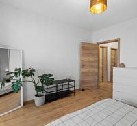 Pokoj v 2pokojovém bytě s bílým nábytkem, zrcadlem a podlahou s dřevěným dekorem.