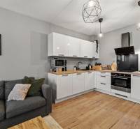 Kuchyně v 2-pokojovém bytě s bílou linkou, šedou sedačkou a podlahou s dřevěným dekorem.