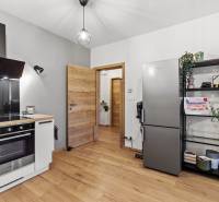 Kuchyně 2pokojového bytu s podlahou s dřevěným dekorem, lednicí a policovými regály.