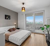 Ložnice v 2-pokojovém bytě s postelí, podlaha s dřevěným dekorem, balkonové dveře.