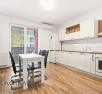 Kuchyně v 2pokojovém bytě s bílými skříněmi a podlahou s dřevěným dekorem.