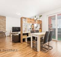 Obývací pokoj s jídelním stolem v 2-pokojovém bytě, podlaha s dřevěným dekorem, knihovna.