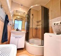 Koupelna v 2-pokojovém bytě se zaskleným sprchovým koutem a pračkou.