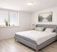 Světlá ložnice v rodinném domě s manželskou postelí a podlahou s dřevěným dekorem.