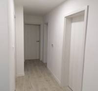 Chodba v rodinném domě s bílými stěnami a podlahou s dřevěným dekorem.