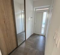 Vstupní chodba rodinného domu s bílými stěnami a skříní v dekoru dřeva.