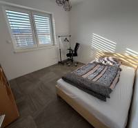 Ložnice v rodinném domě s postelí, pracovní židlí a velkým oknem.