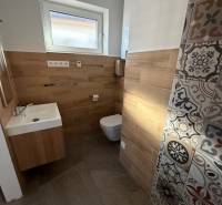 Koupelna v rodinném domě s umyvadlem, WC a podlahou s dřevěným dekorem.