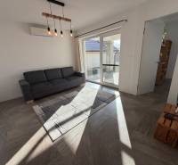 Obývací pokoj v rodinném domě s pohovkou, krémovými závěsy a prosklenými dveřmi na terasu.