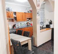 Kuchyně v rodinném domě s obloukovým vstupem, dřevěné skříňky a černé podlahy.