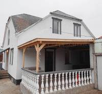 Rodinný dům ve Vizsoly s terasou, bílou fasádou a dřevěným přístřeškem.