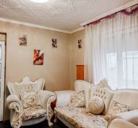 Obývací pokoj rodinného domu s ornamentálním nábytkem a fotografiemi na stěnách.