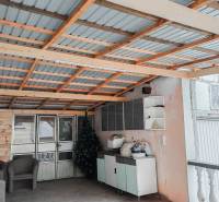 Rodinný dům: Přístřešek s kovovou střechou, ratanová křesla, umělé stromky, úložné prostory.