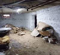 Suterén rodinného domu s hliněnou podlahou, několika krabicemi a dřevem.