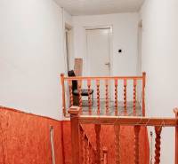 Schodiště s dřevěným zábradlím v rodinném domě, bílé stěny, osvětlení se žárovkou.