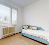 Pokoj se světlou pohovkou, velkým oknem a radiátorem ve čtyřpokojovém bytě.