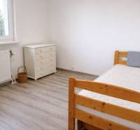 Pokoj v 3-pokojovém bytě s podlahou s dřevěným dekorem, postelí a komodou.