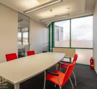 Kanceláře se skleněnou stěnou, bílým stolem a červenými židlemi.