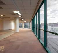 Prostorné kanceláře s velkými okny a rozložitými sloupy, výhled na ulici.