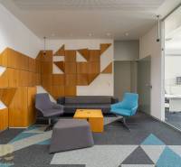 Interiér kanceláří s barevným sezením, sklem a geometrickými dřevěnými panely.